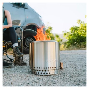 A woman enjoys a campfire near her van equipped with a Solo Stove Stainless Steel Ranger.