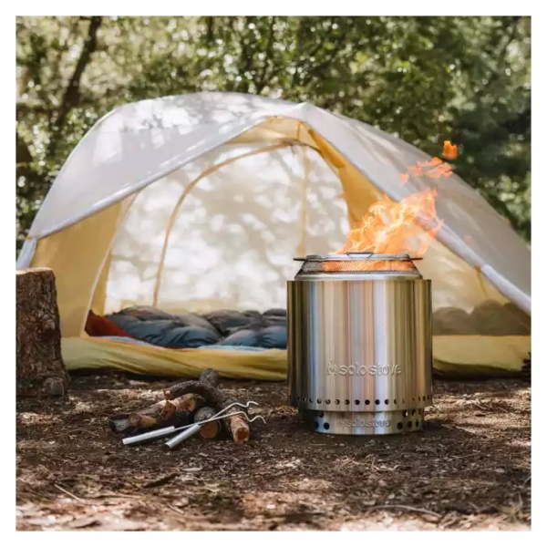 A portable camp stove with a tent in the woods.