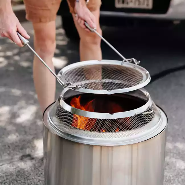 A person holding a portable stainless steel fire pit.