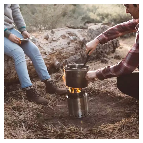 Two individuals using the Solo Stove Stainless Steel Titan Camp Stove to cook in the woods.