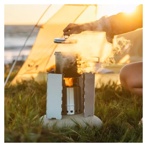 A woman is cooking on a Solo Stove Stainless Steel Titan Camp Stove in front of a tent.