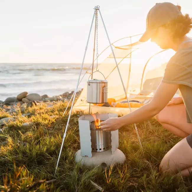 A woman is cooking on a solo camp stove near the ocean.
