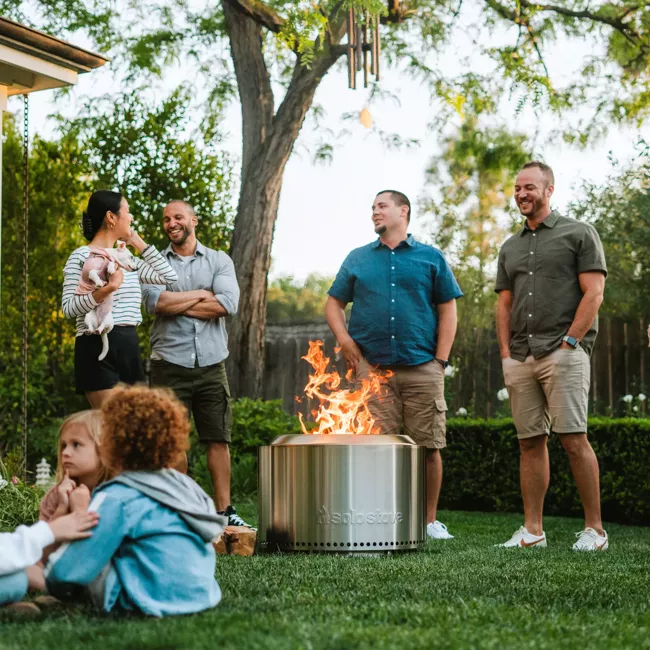 A group of people standing around a portable fire pit in a backyard.