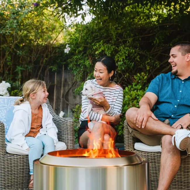 A family enjoys a cozy backyard fire pit experience with a portable and "smokeless" Solo Stove Yukon Essential Bundle 2.0.