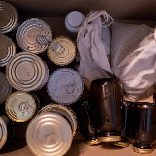 A box filled with various cans and bottles, emphasizing the history of emergency food storage.