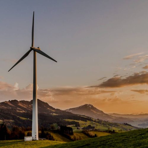 A wind turbine harnesses sustainable energy on a grassy hill at sunset, emphasizing its importance in the modern world.