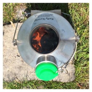 A camp stove for emergency food storage with a green lid sitting on the grass.