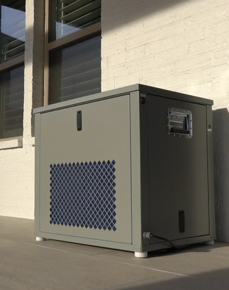 A portable air conditioner, suitable for emergency food storage, sitting on the side of a building.