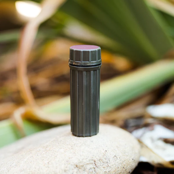 A small bottle of safety weatherproof matches, with a waterproof case, sitting on top of a rock.