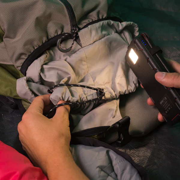 A person putting a cell phone into a backpack equipped with the QuadraPro Solar Power Bank.