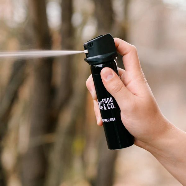 A person spraying a black spray bottle in the woods, using the LifeShield Self Defense Kit.