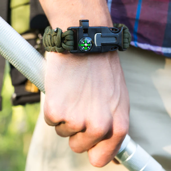 A person holding a Frog & Co. Paracord Survival Bracelet with a compass on it.