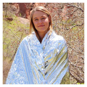 A woman, wrapped in a silver Emergency Survival Blanket, standing in the woods.
