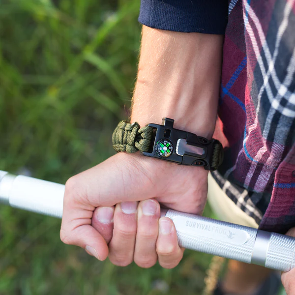 A man holding a Frog & Co. Paracord Survival Bracelet in the grass.