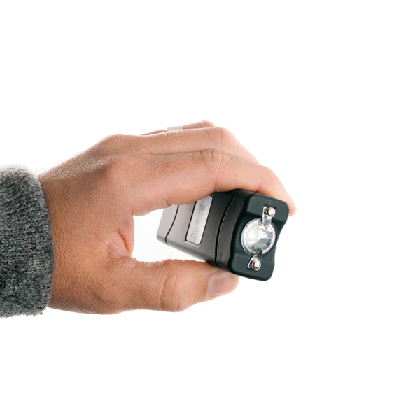 A hand holding a small flashlight for Self Defense on a white background.