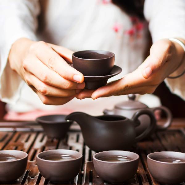 A woman is holding a cup of tea on a table, showcasing the right way to serve tea.